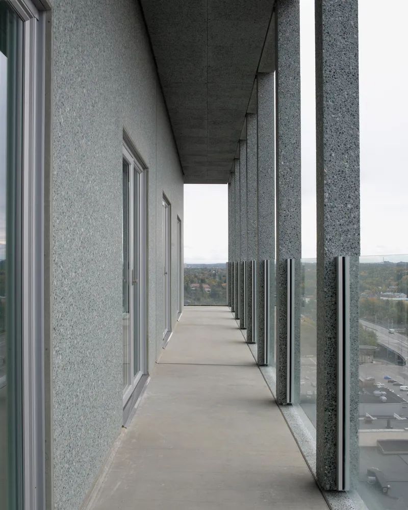 Exterior balcony corridor with exposed aggregate concrete ceiling and glass balustrade panels looking toward the horizon