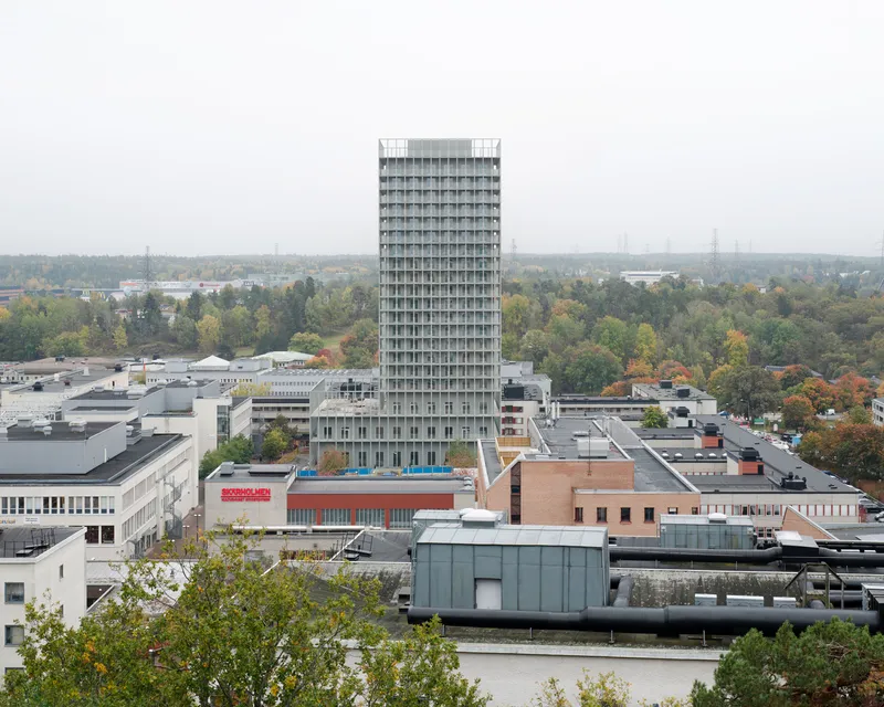 Aerial view of the residential tower standing above surrounding industrial and commercial rooftops with fall foliage beyond