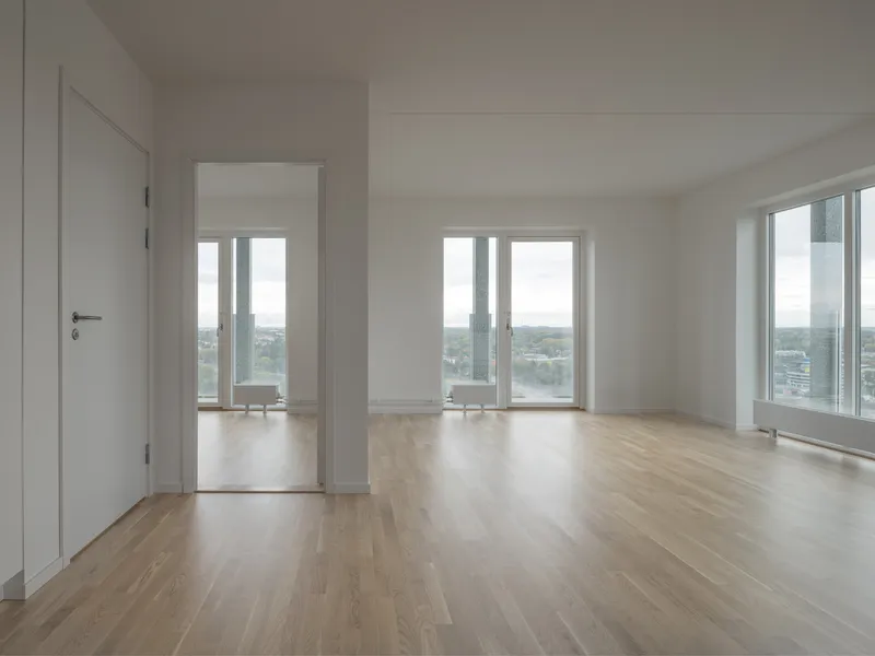 Empty apartment interior with pale wood flooring and white walls overlooking water through three tall windows