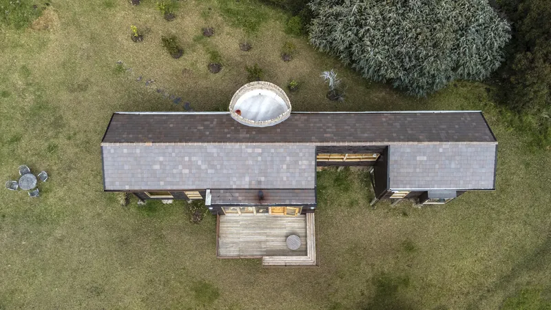 Overhead drone view showing the T-shaped plan with timber shingle roofing and skylight dome