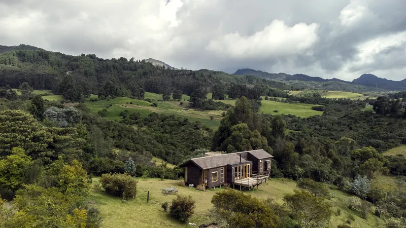 Aerial view of the timber cabin set within rolling green hills beneath dramatic storm clouds