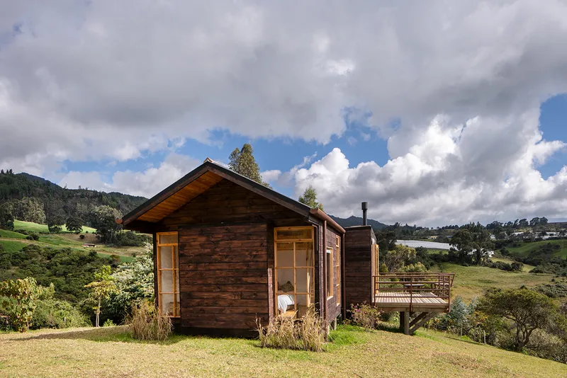 Dark wood cladding on the gabled volume with an exterior deck under afternoon clouds