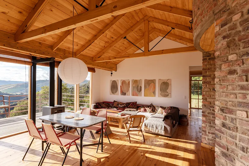 Open living space with vaulted timber ceiling, brick fireplace wall and sunlight across the wooden floor
