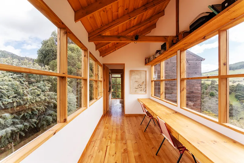 Interior corridor with exposed timber trusses, pine flooring and floor-to-ceiling windows framing the hillside