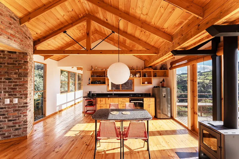 Kitchen and dining area under exposed timber roof trusses with built-in cabinetry and glazed doors