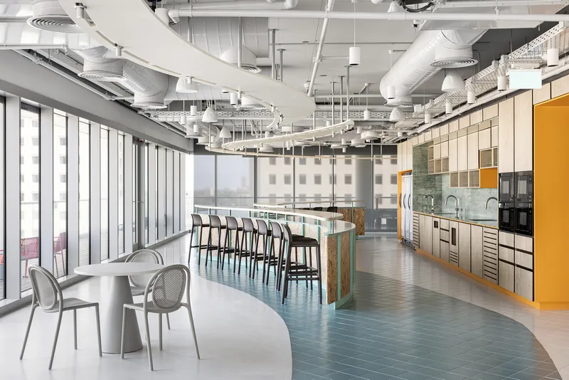 Open-plan office pantry with exposed ceiling ducts, teal herringbone flooring and a yellow accent wall