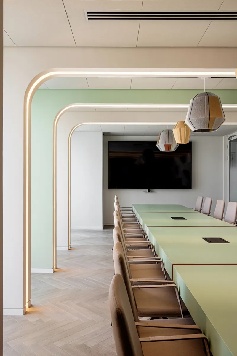 Conference room with rounded illuminated portal frames and a pale green table under pendant lights