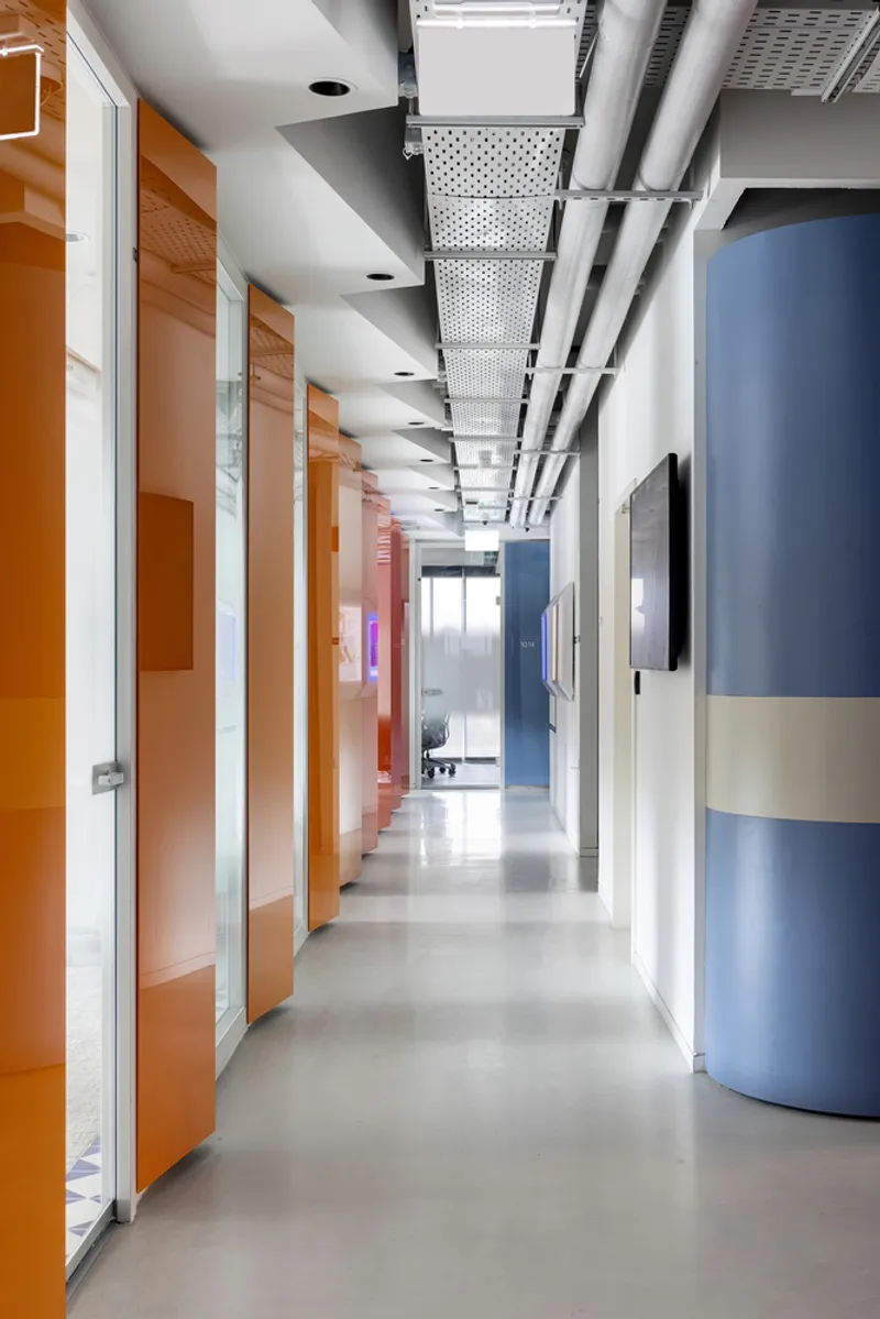Corridor with orange glass doors, perforated ceiling panels and a blue cylindrical column