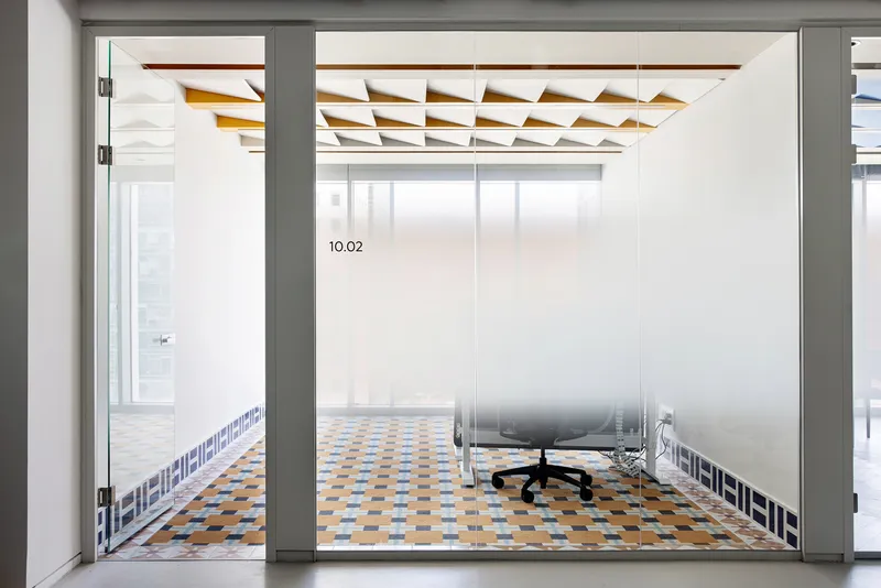 Glass-walled office with patterned tile floor and faceted timber ceiling panels above