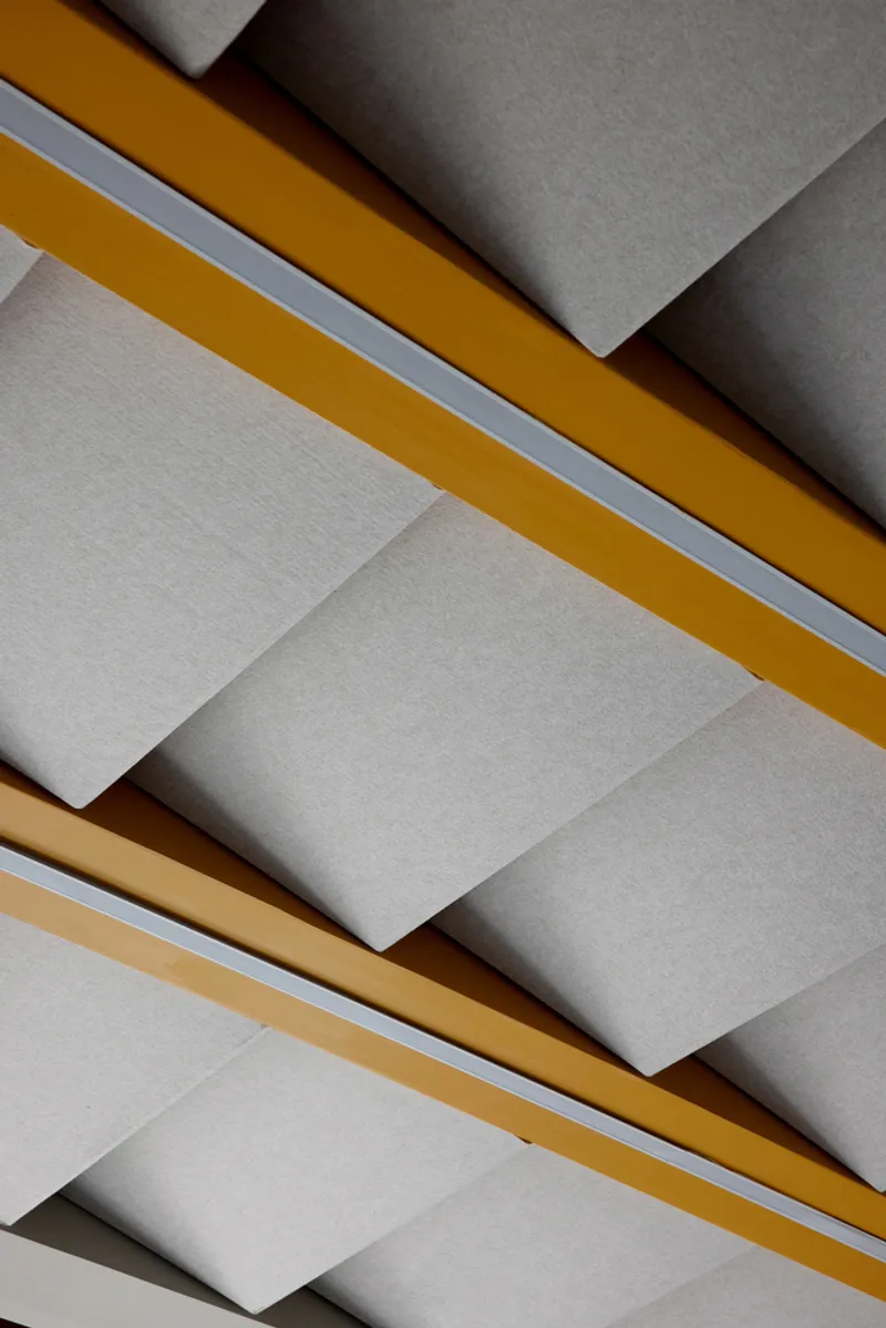 Ceiling detail showing white panels with yellow and tan timber beams casting angular shadows