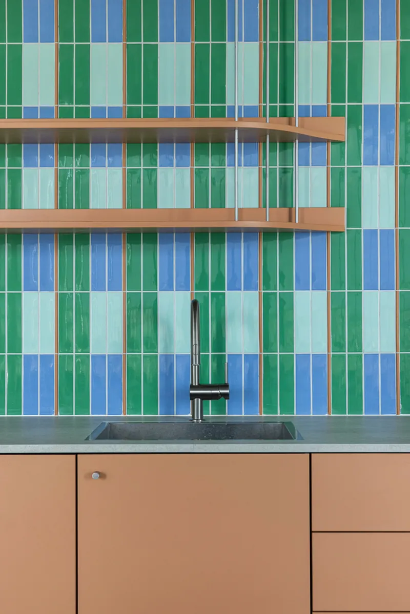 Kitchen backsplash with vertical stripe tiles in green and blue with timber shelves and tan cabinetry