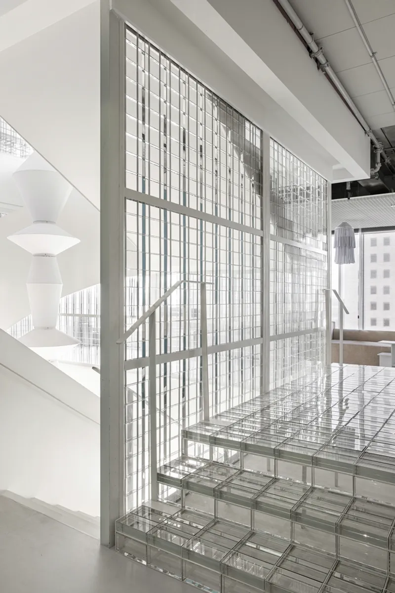 Glass block staircase ascending alongside a gridded translucent screen wall with white railing