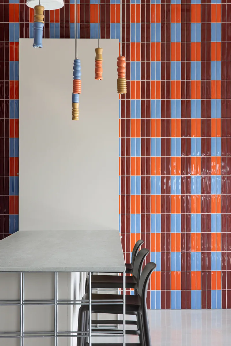 Dining area with blue and orange checkered tile wall and ceramic pendant lights above a table