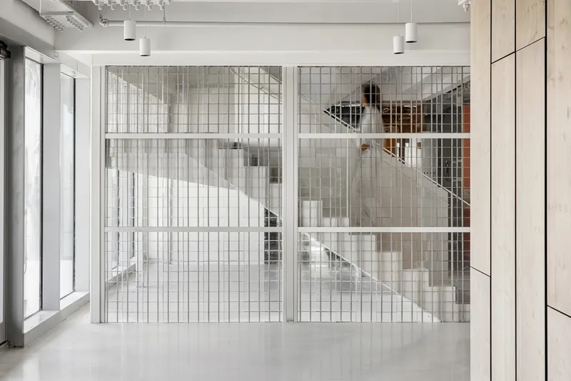 Full-height wire mesh enclosure framing the central staircase visible through translucent glass walls under suspended ceiling fixtures