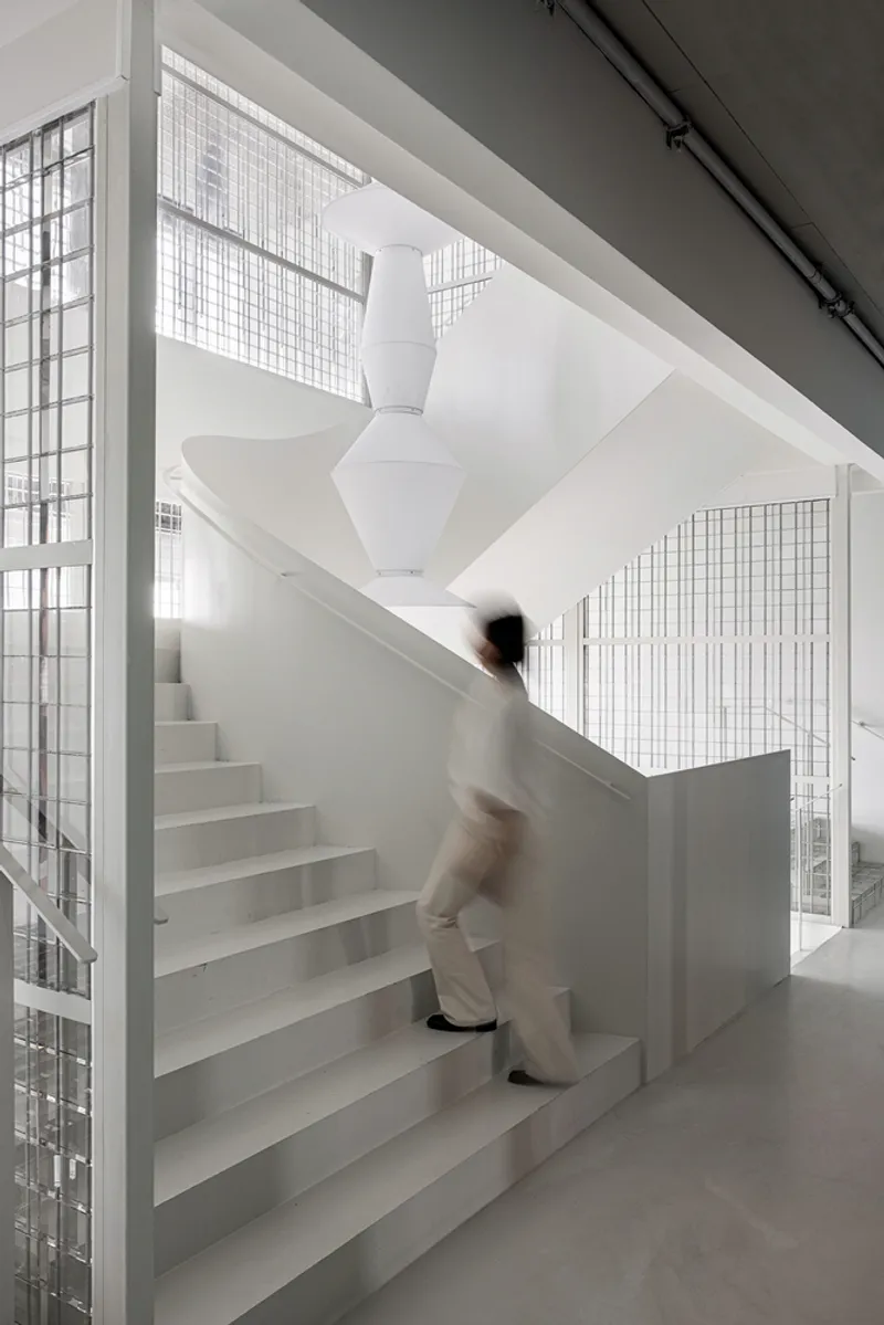 Central staircase with a figure in motion ascending the steps behind wire mesh partitions and white sculptural column overhead