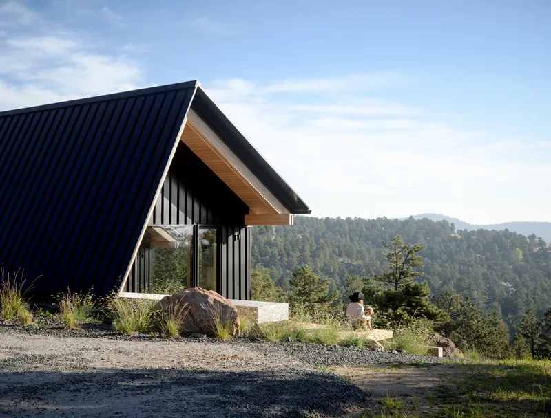 Entrance elevation showing vertical siding and exposed timber eave with a figure seated on the low retaining wall