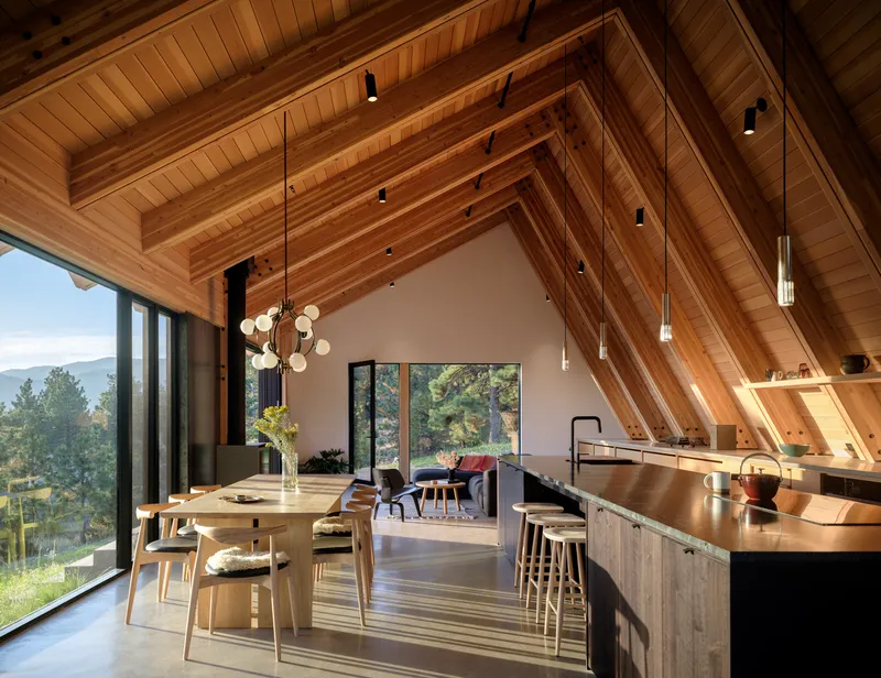 Open kitchen and dining area with exposed timber beams and vaulted ceiling under pendant lighting