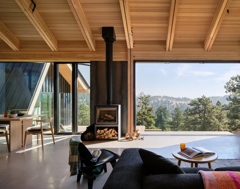 Living room with freestanding wood stove and panoramic opening framing forested hillside views