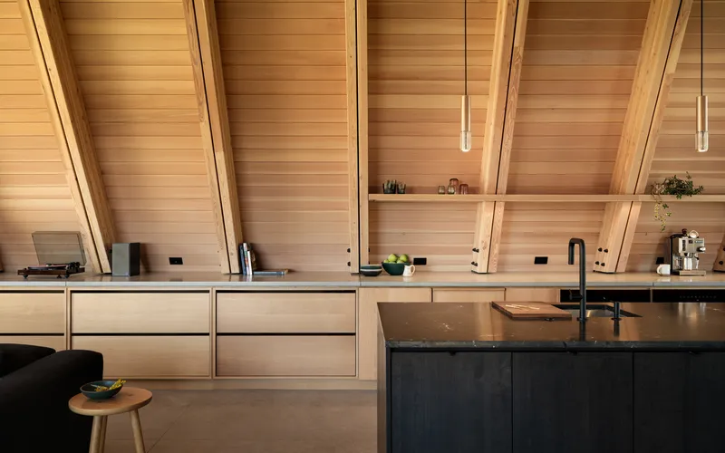 Kitchen cabinetry detail with timber shelving recessed into the sloped ceiling structure at evening