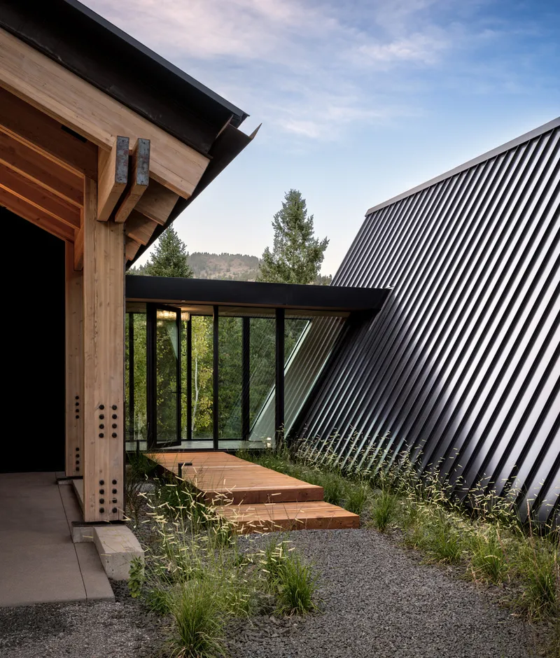 Exterior courtyard with timber entry volume, corrugated metal facade, and gravel landscape bed with native grasses
