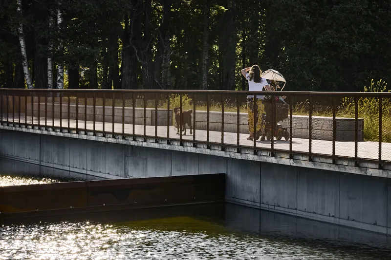 Concrete bridge with mesh railings and pedestrians walking with a dog in afternoon light