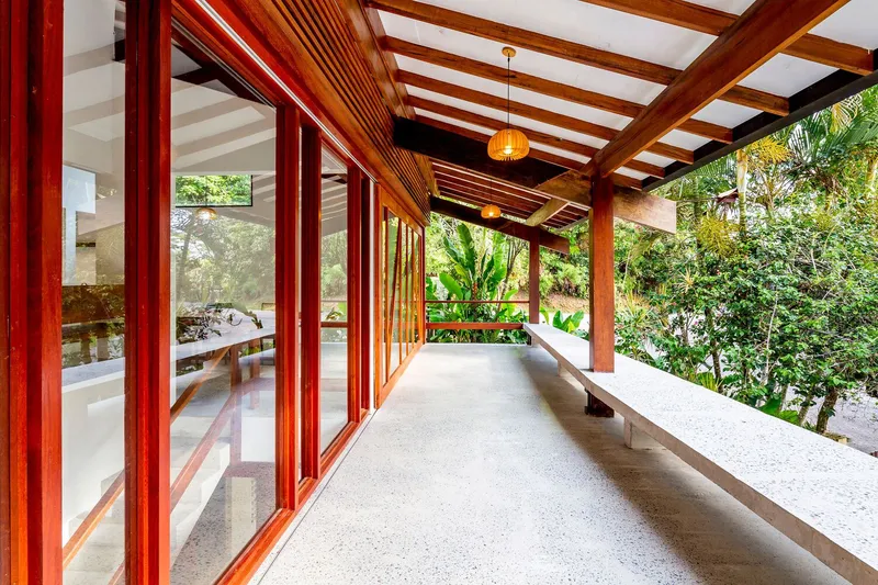 Covered corridor with timber-slatted screens and exposed rafters overlooking tropical garden foliage
