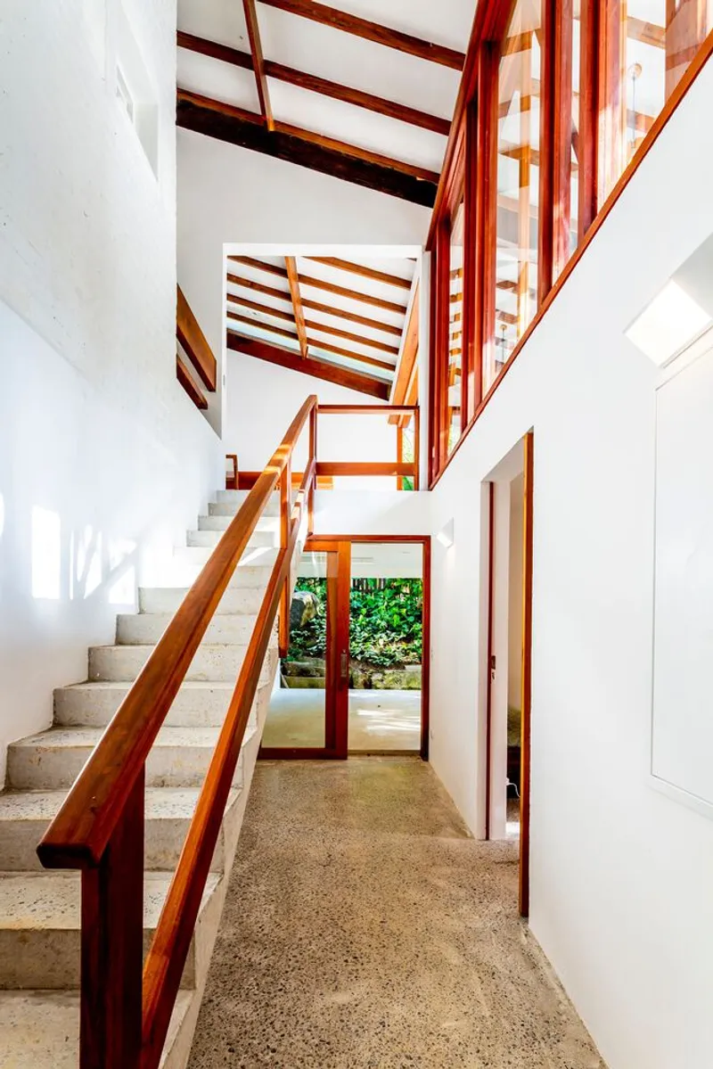 Stairwell with timber railings and terrazzo treads beneath exposed timber roof structure and clerestory glazing