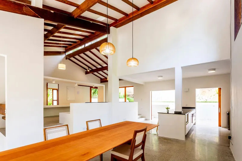 Open-plan dining and kitchen space with timber table under exposed ceiling beams and pendant lights