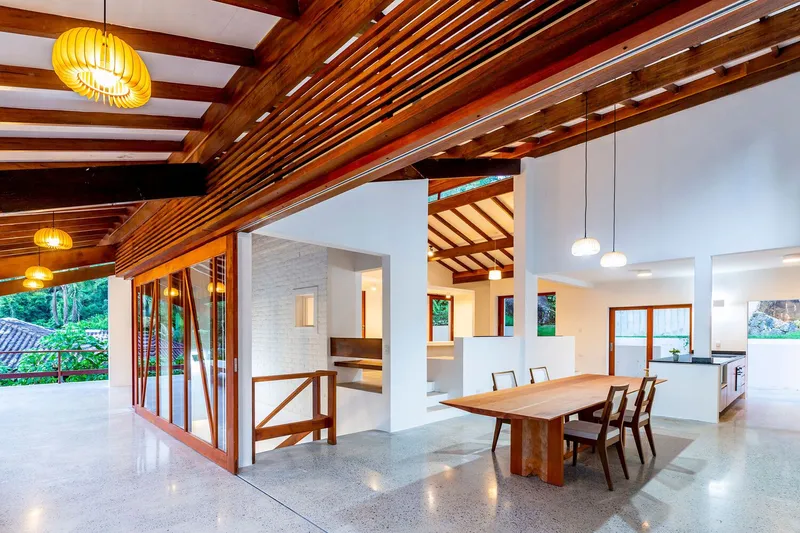 Open-plan living space with timber ceiling beams, terrazzo flooring, and pendant lights at dusk