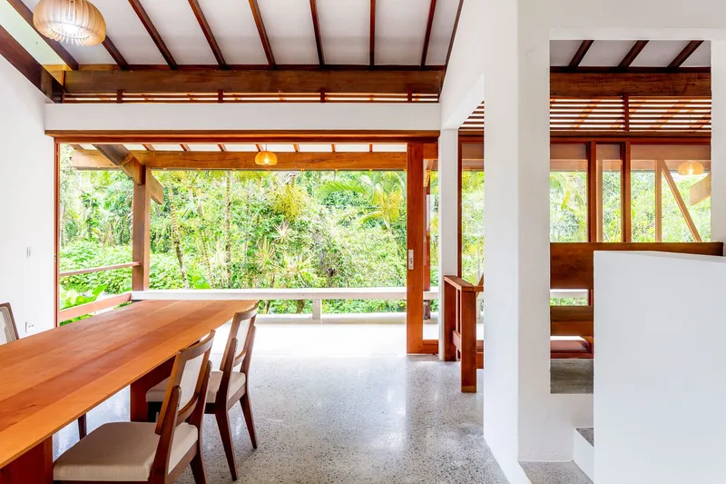 Dining area with timber table and exposed beam ceiling opening to lush garden through full-height glazing