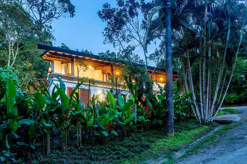Two-story volume with overhanging timber roof nestled among tropical palms and banana plants at twilight