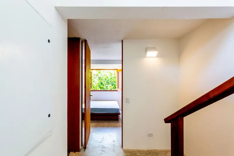 White interior hallway with timber handrail and deep red doorframe opening to a bedroom with terrazzo flooring