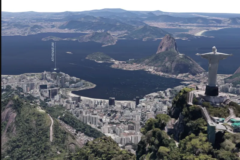 Aerial view of dense urban fabric nestled between green peaks, bay and monument statue