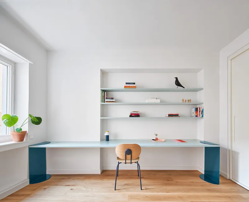 Study nook with built-in desk and shelving in light blue, wooden chair, and potted plants on windowsill