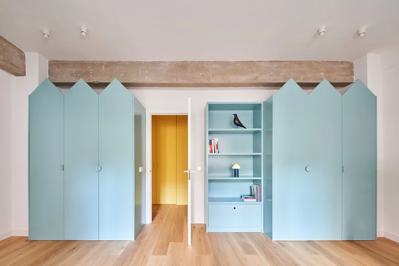 Room with pale blue house-shaped wardrobe panels flanking central doorway, exposed timber beam above, and built-in shelving