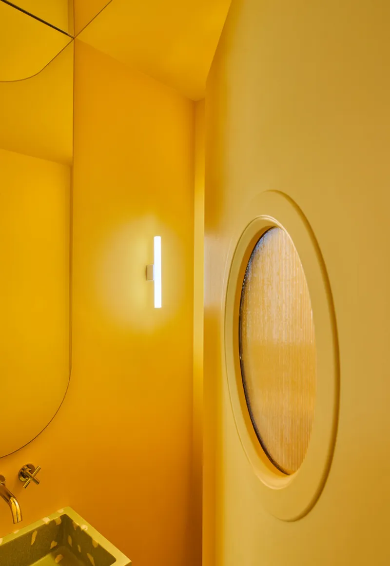 Yellow bathroom corner showing oval mirror with cane insert and vertical luminaire beneath curved ceiling