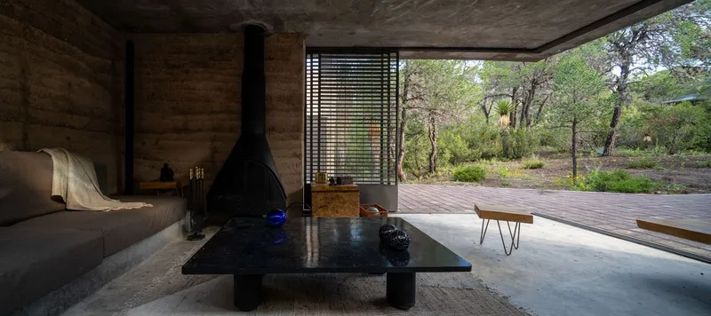 Interior space opening to timber deck terrace through slatted metal screen with freestanding fireplace