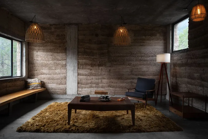 Interior lounge with rammed earth walls, woven pendant lights, and a single concrete column