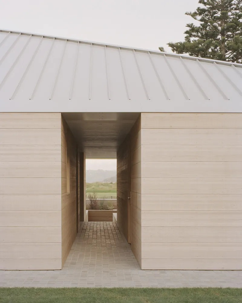 Covered passage through horizontal timber cladding with paved brick floor and view to distant landscape