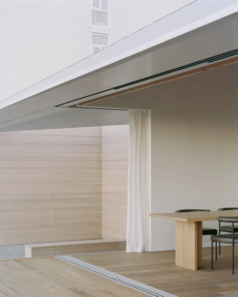 Corner detail of metal standing seam roof meeting timber column and sheer white curtain