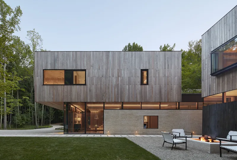 Rear facade with cantilevered timber-clad upper volume over limestone base and glazed openings at dusk
