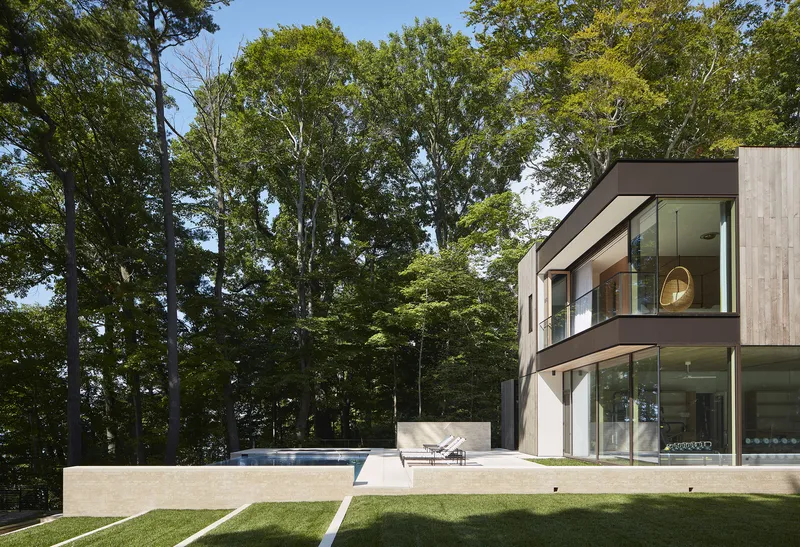 Rear terrace with cast concrete pool deck and two-story glass facade overlooking wooded hillside