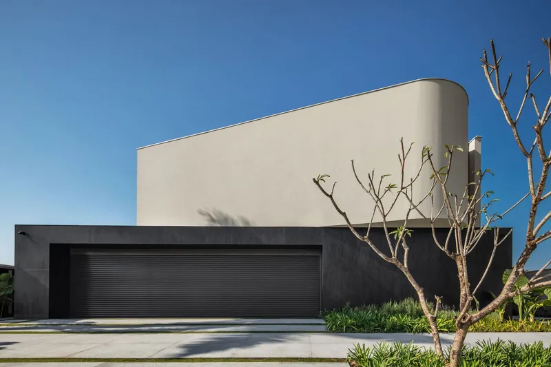 Street view of the two-tone facade with black garage door and bare branched tree under blue sky