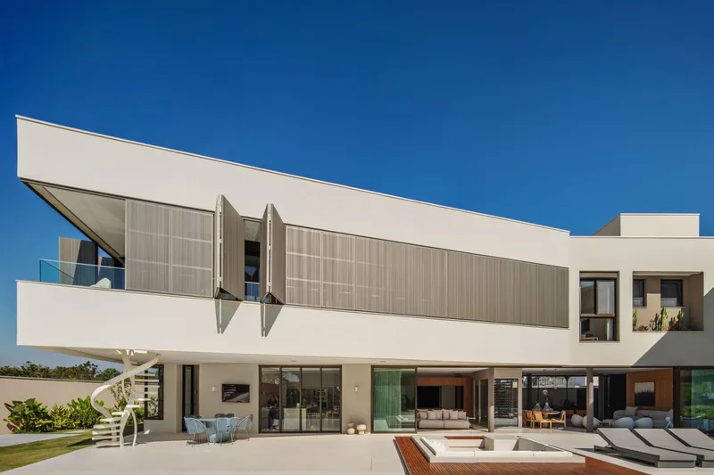 Rear facade with cantilevered upper volume, operable louvered shutters, and terrace with loungers overlooking the pool