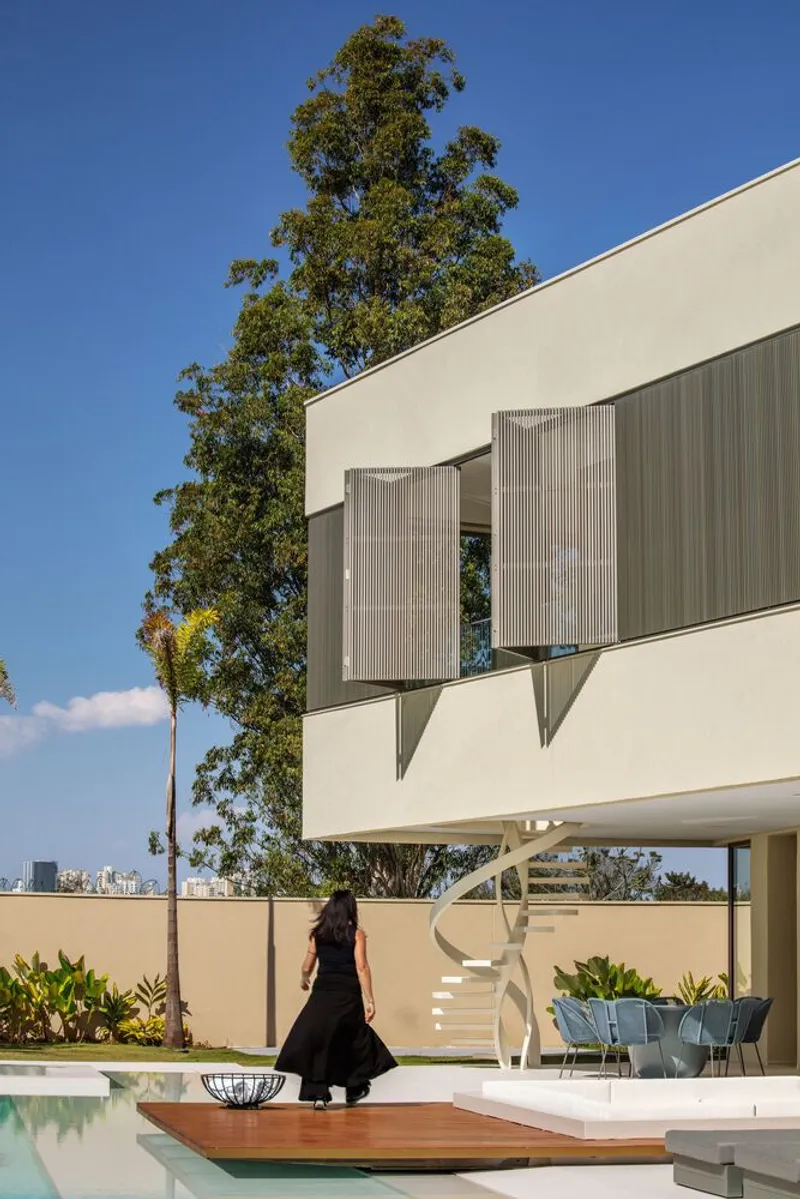 Woman in black walking past white spiral stair below cantilevered volume with vertical timber screens