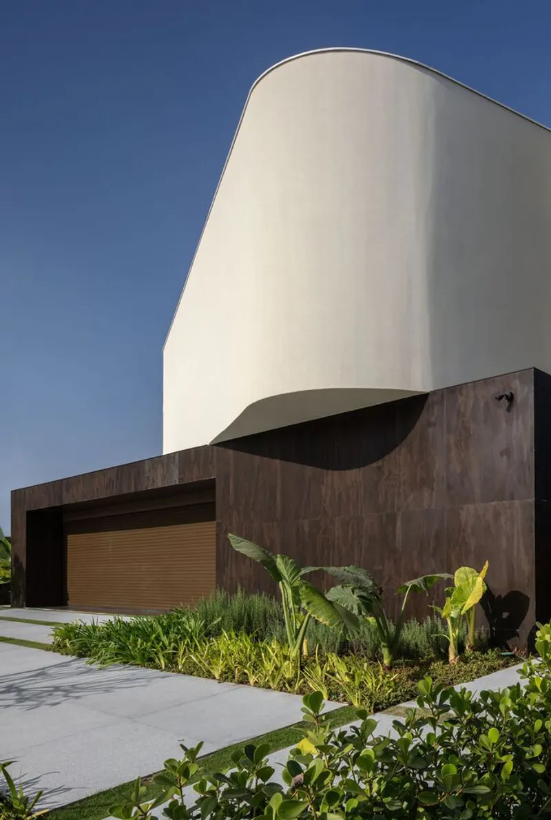 Curved white stucco volume above a timber-clad base with planted bed in bright daylight
