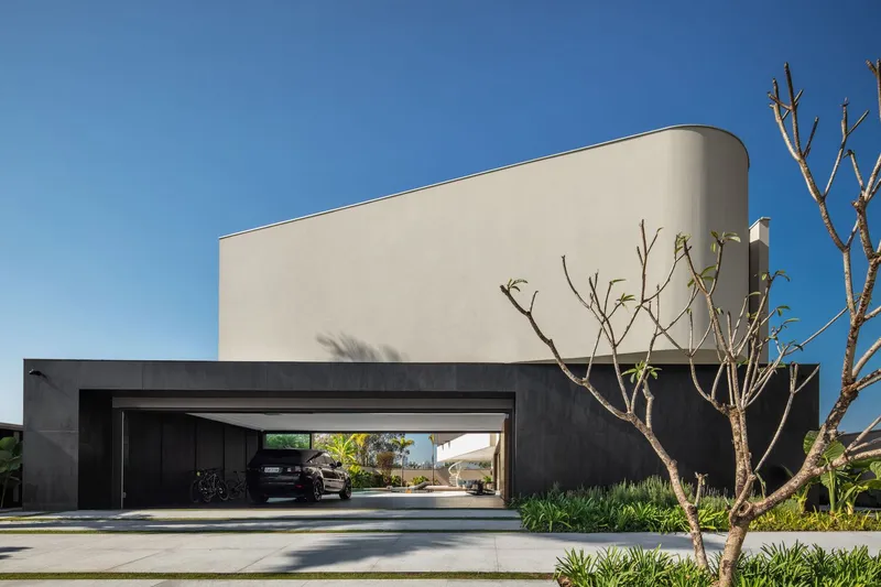 Front elevation with open garage door revealing vehicles parked inside beneath the curved stucco volume