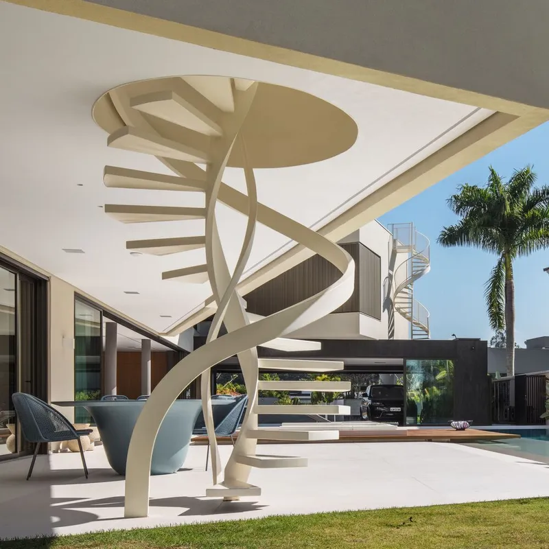 White spiral stair with circular ceiling cutout under covered terrace beside palm trees