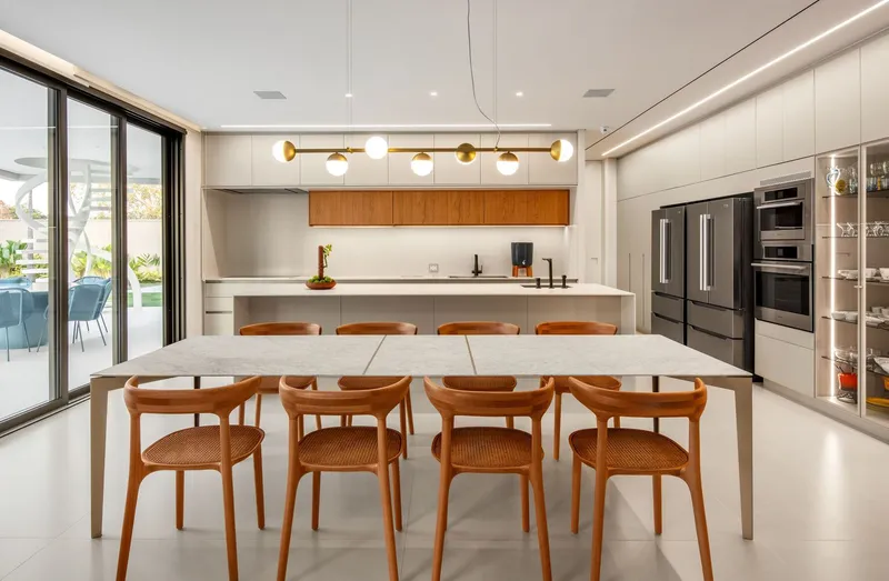 Kitchen and dining space with timber chairs around a white table under linear pendant lighting
