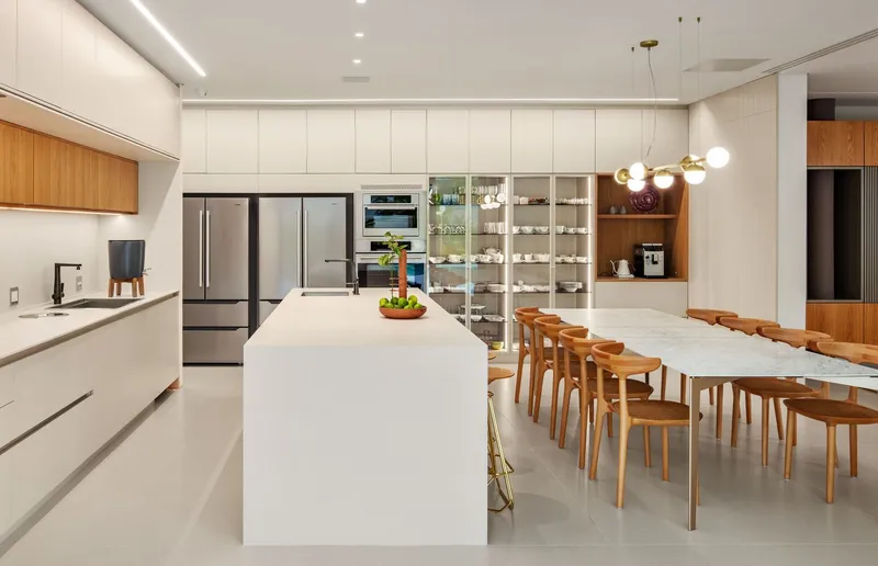 Kitchen with white island and glass display shelves adjoining a timber dining table